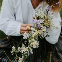 En person i vit blus och randig kjol håller en bukett med sju sorters blommor, en midsommartradition.