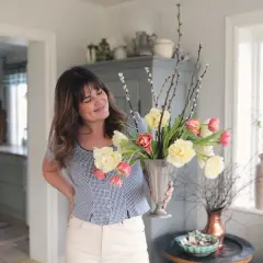 En kvinna håller en silvervas fylld med tulpaner och videkissar. Vattnet i vasen håller blommorna fräscha.