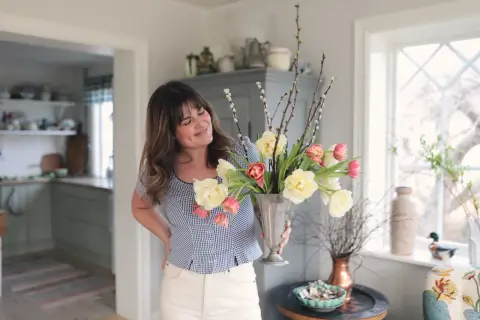 En kvinna håller en silvervas fylld med tulpaner och videkissar. Vattnet i vasen håller blommorna fräscha.