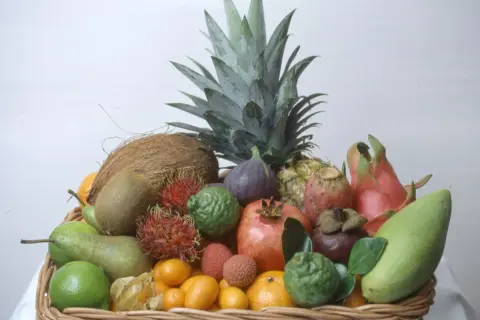En korg fylld med exotiska frukter, inklusive en ananas som ser ut att vara redo att odla. Här finns även kokosnöt, kiwi, rambutan, granatäpple och mango.