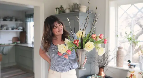 En kvinna håller en silvervas fylld med tulpaner och videkissar. Vattnet i vasen håller blommorna fräscha.