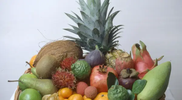 En korg fylld med exotiska frukter, inklusive en ananas som ser ut att vara redo att odla. Här finns även kokosnöt, kiwi, rambutan, granatäpple och mango.