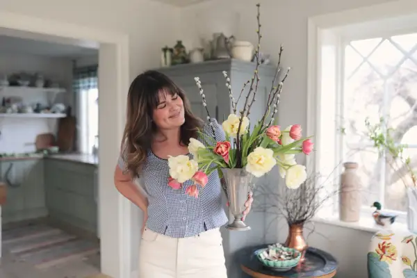 En kvinna håller en silvervas fylld med tulpaner och videkissar. Vattnet i vasen håller blommorna fräscha.